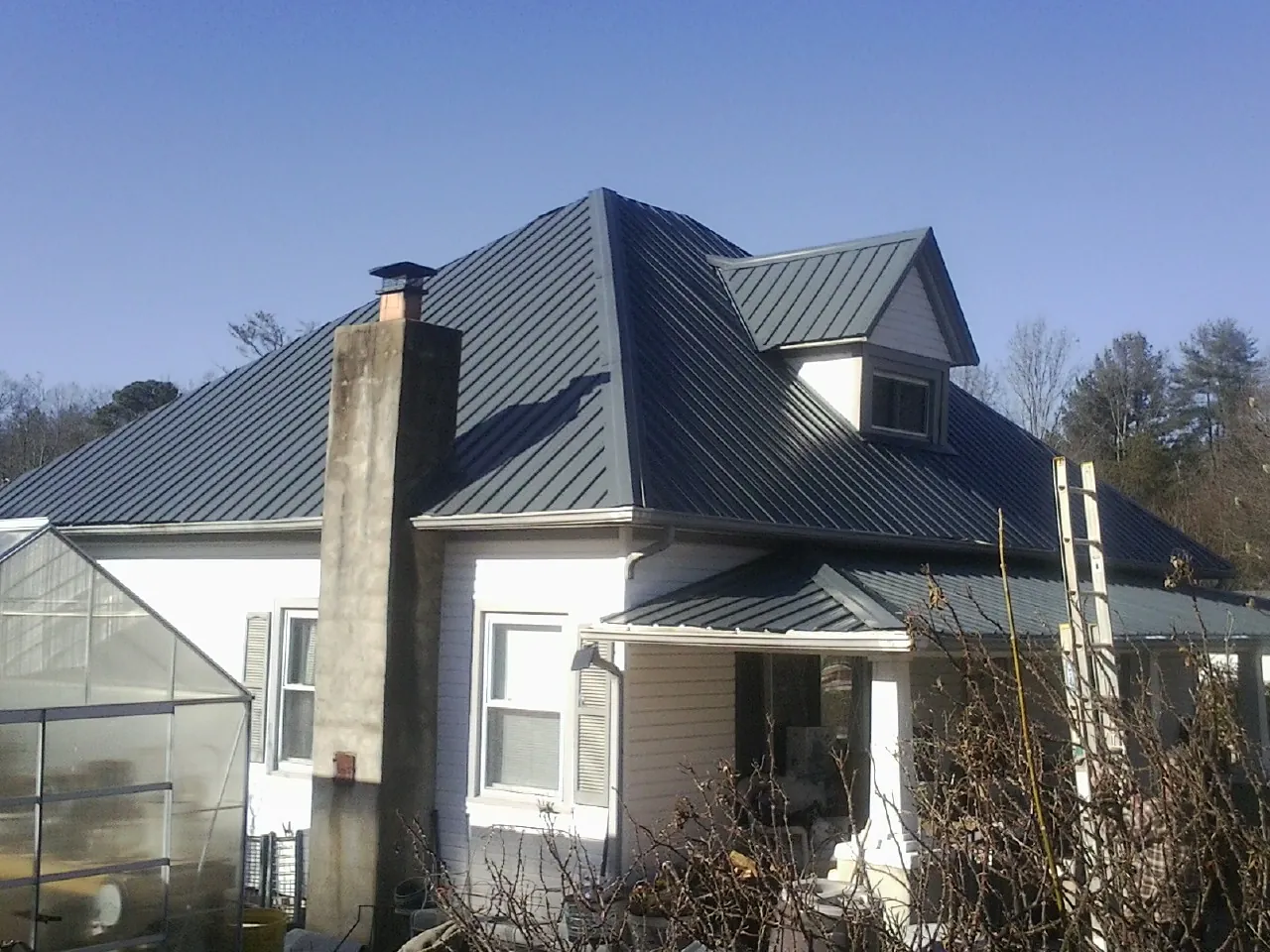 Dark blue standing seam metal roof on a white farmhouse with dormer — Slate & Tile Roof Repair by Roofing Brothers in Enville
