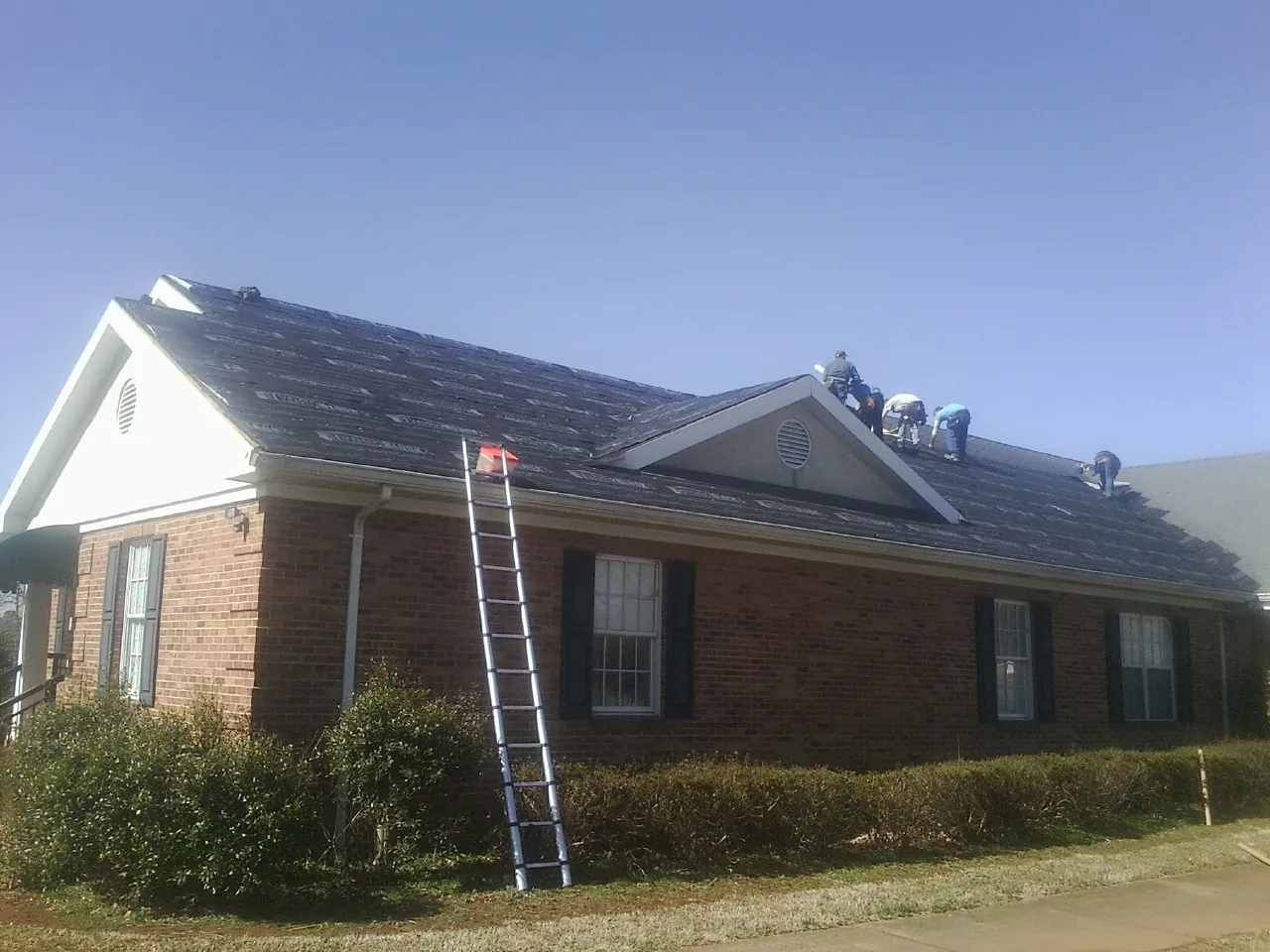Crew tearing shingles off a brick ranch roof with a ladder set — Emergency Roof Repair work by our crew in Enville