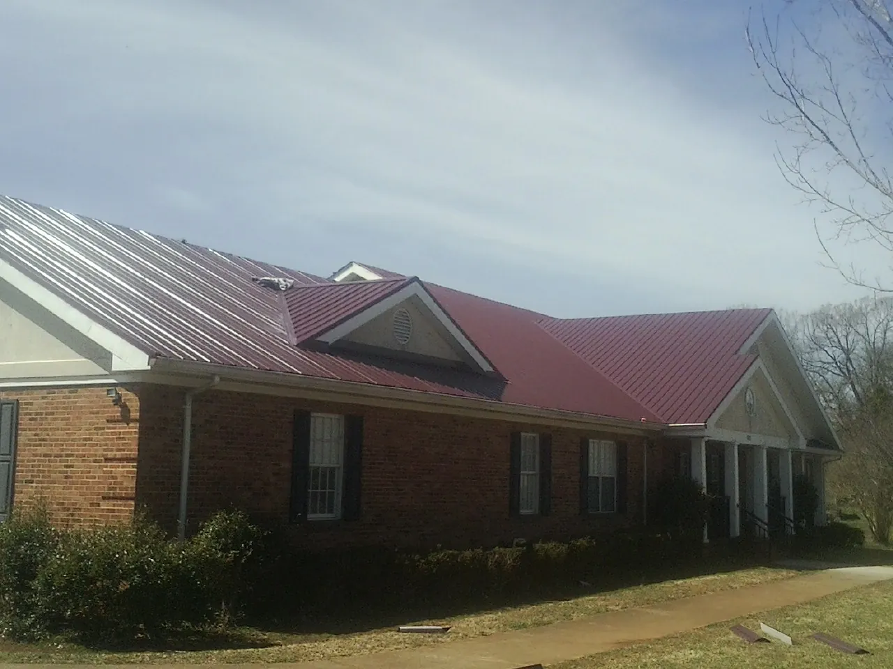 Red metal roof with gabled entries on a long brick building, from a Hail Damage Roof Repair job in Enville