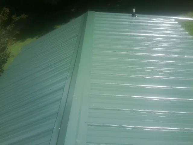 New green metal panels meeting at the ridge of a roof — Flat Roof Repair work by our crew in Enville