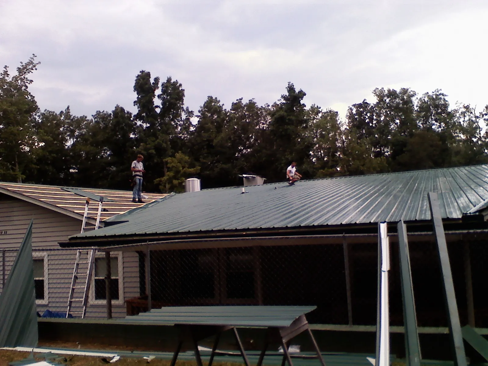 Two roofers installing green metal panels above a covered porch in Enville