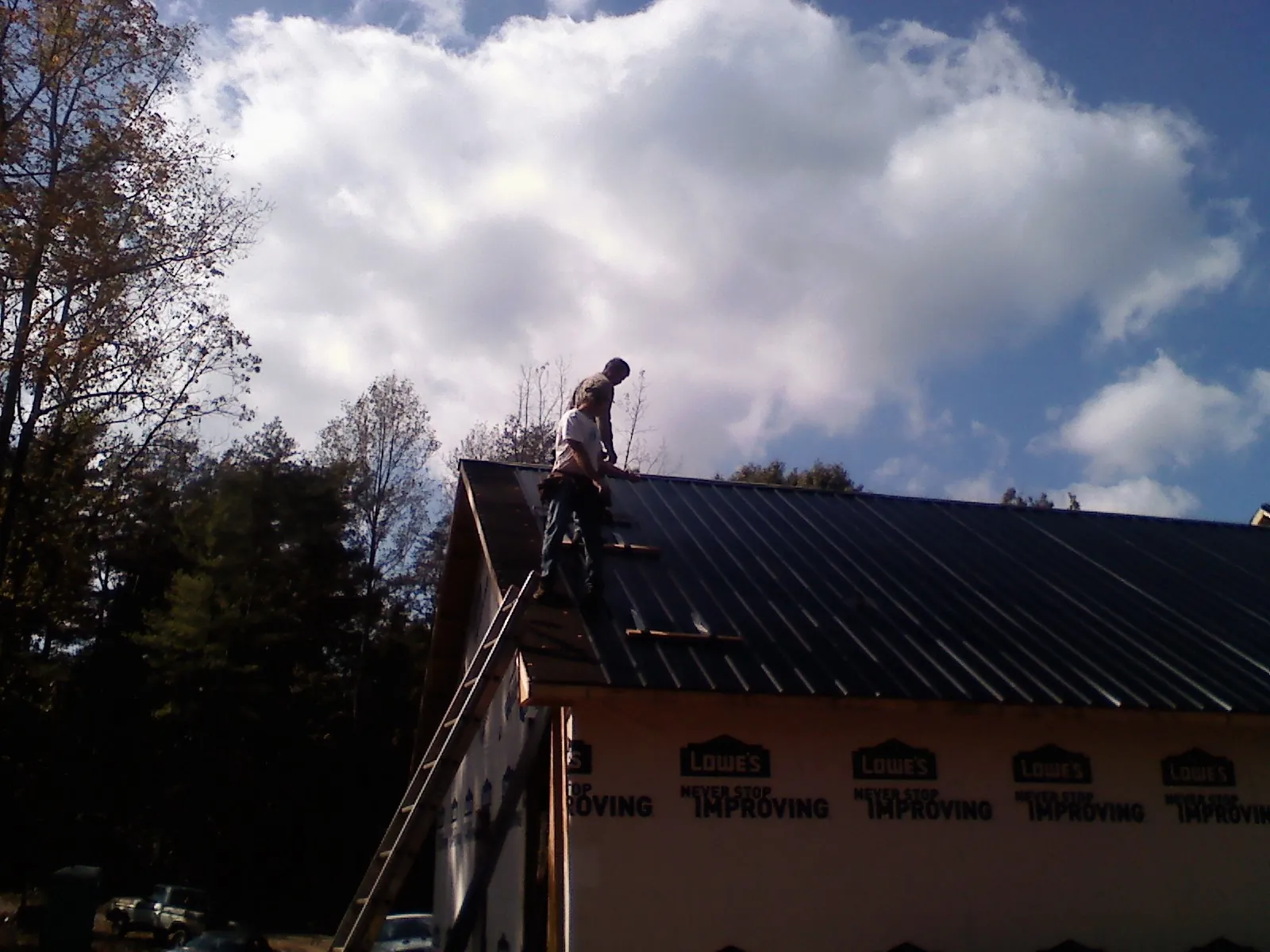 Roofer fastening dark metal panels high against a cloudy sky, from a Roof Inspection job in Enville