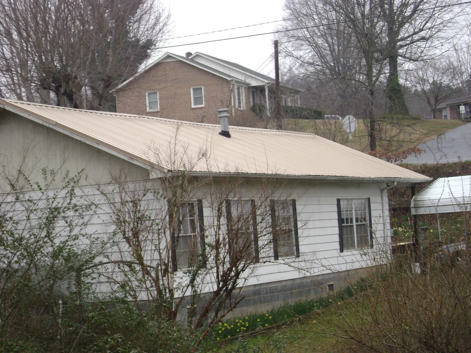 Tan metal roof on a white sided house set into a hillside — Commercial Roofing by Roofing Brothers in Enville