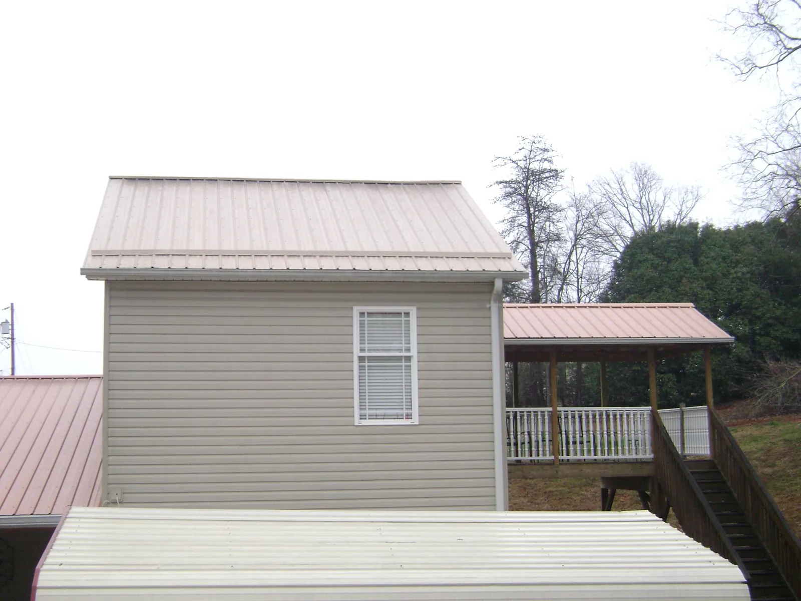 Tan metal roofs on a two story addition and attached porch, from a Roof Replacement job in Enville